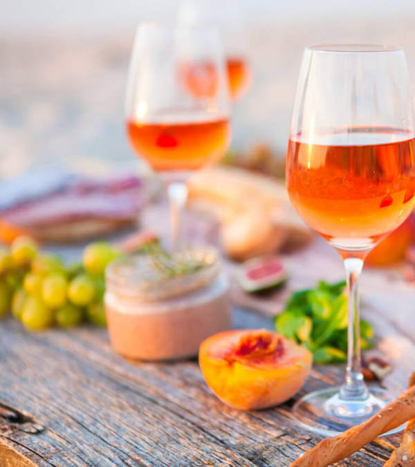 KI generiert: Weingläser mit Rosé auf einem Holztisch, dazu Früchte und Wurstwaren.