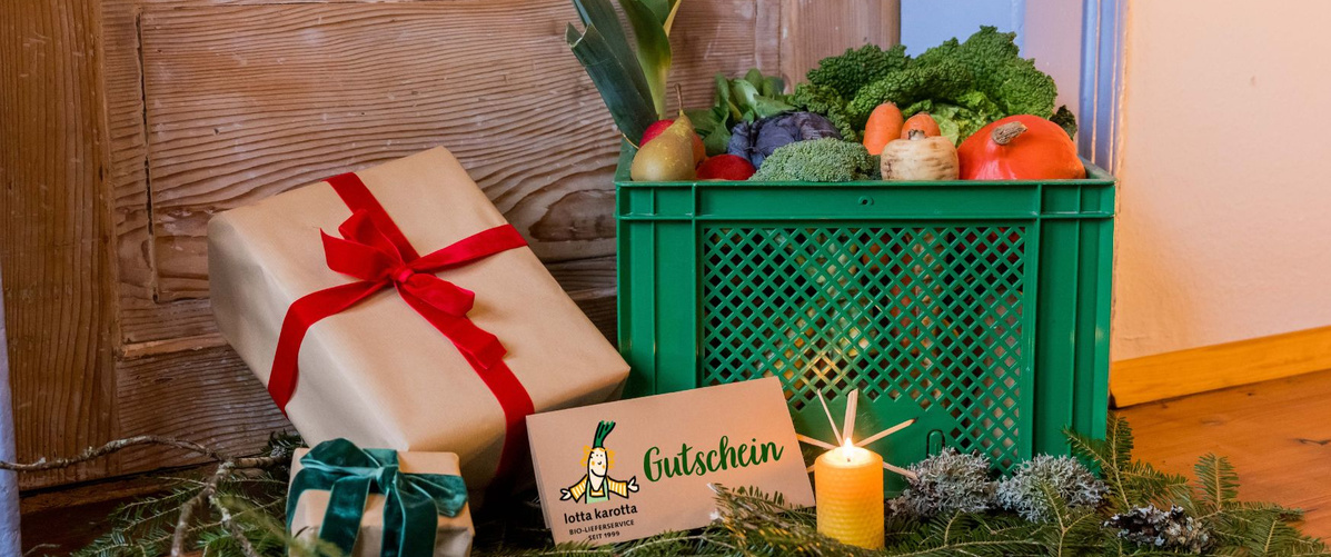 KI generiert: Geschenkverpackungen, Gemüsekorb und Gutschein mit Kerze neben einer Holztür. Text im Bild: "Gutschein, lotta karotta".