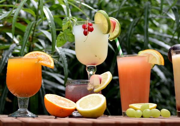 KI generiert: Verschiedene bunte Cocktails und Früchte vor einem Hintergrund mit grünen Blättern. Kein Text enthalten.