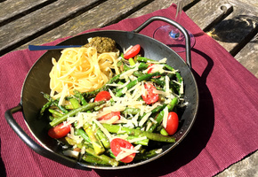 KI generiert: Ein Gericht mit Nudeln, grünem Spargel, Kirschtomaten und Käse auf einem Tisch.