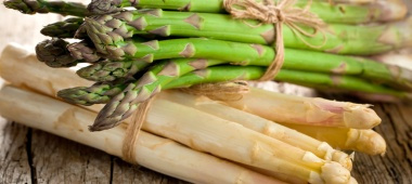 KI generiert: Grüner und weißer Spargel, gebündelt und auf einer Holzoberfläche liegend.