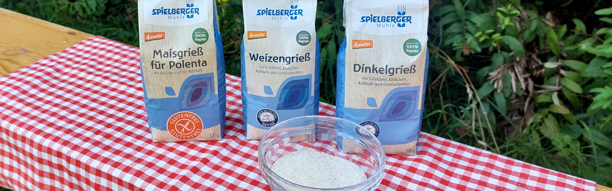 KI generiert: Drei Packungen Spielberger Grieß auf kariertem Tuch, Text: "Maisgrieß für Polenta," "Weizengrieß," "Dinkelgrieß".