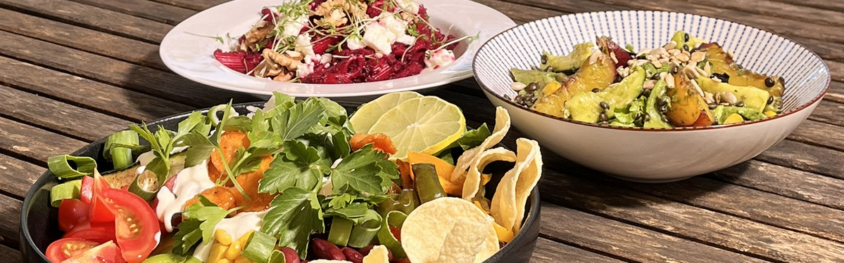 KI generiert: Drei bunte Salate auf einem Holztisch, dekoriert mit frischen Kräutern und Toppings.