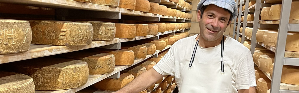 KI generiert: Ein Mann steht lächelnd in einem Lager voller Käselaibe.