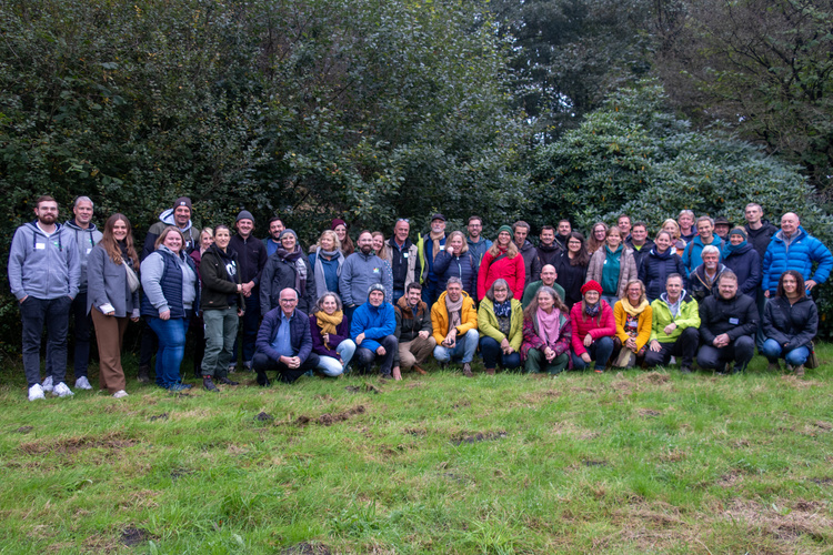 KI generiert: Eine große Gruppe von Menschen steht zusammen auf einer Wiese vor Bäumen.