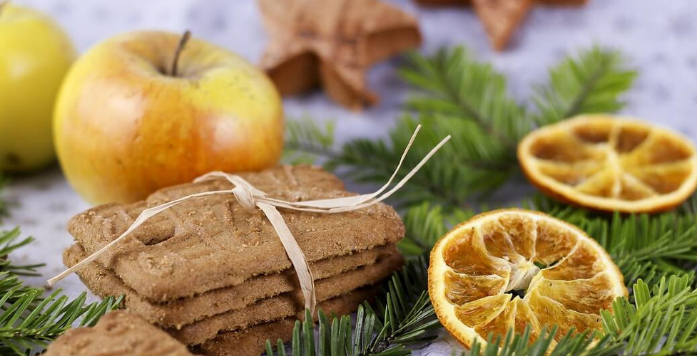 Äpfel, getrocknete Orangenscheiben und Spekulatius auf Zweigen angerichtet