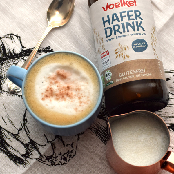 KI generiert: Tasse Cappuccino mit Haferdrink von Voelkel, Löffel und Milchkännchen.