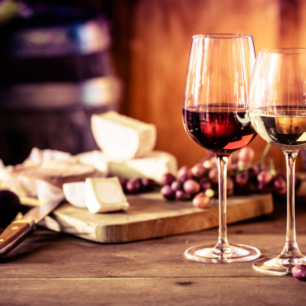 KI generiert: Zwei Weingläser, eines mit Rotwein und eines mit Weißwein, auf einem Tisch mit Käse und Trauben.