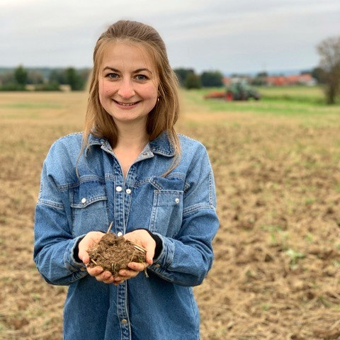 KI generiert: Frau hält Erdballen auf einem Feld in den Händen und lächelt.