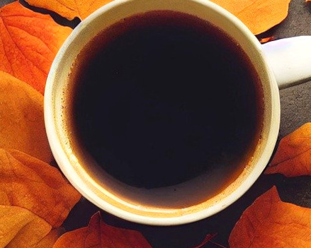 KI generiert: Eine Tasse Kaffee umgeben von orangefarbenen Herbstblättern.