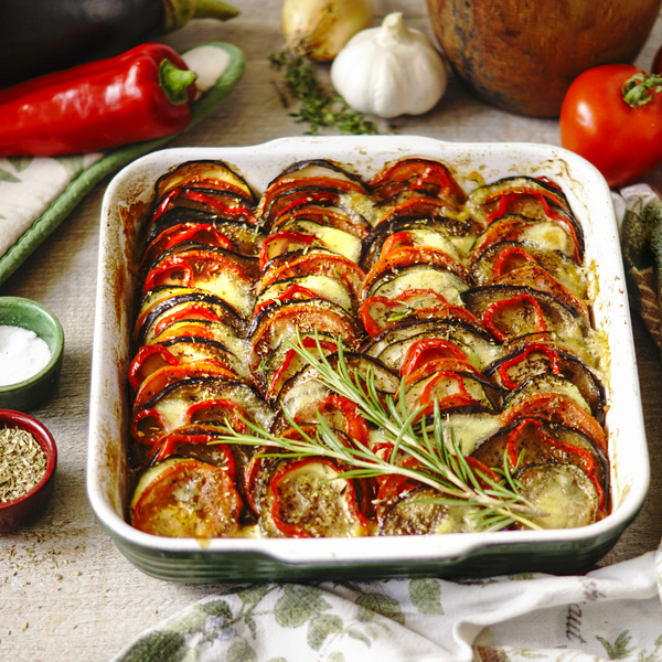 KI generiert: Ein Gemüseauflauf aus Tomaten, Auberginen und Zucchini in einer Auflaufform, garniert mit Rosmarin.

