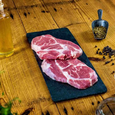 KI generiert: Zwei rohe Fleischstücke auf Schieferplatte, umgeben von Pfefferkörnern und Ölflasche auf Holztisch.