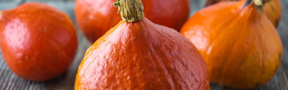 KI generiert: Mehrere orangefarbene Hokkaido-Kürbisse auf einer Holzoberfläche.